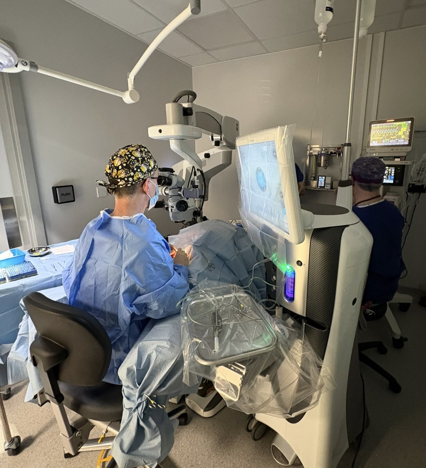 Dr Richard Everson performing cataract surgery at the Zeiss operating microscope while the team follows on screen